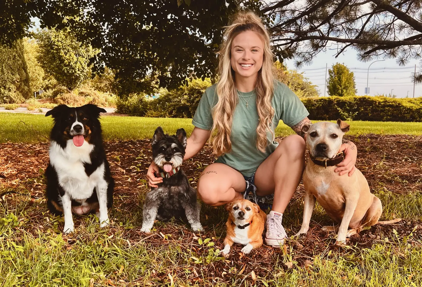 Kaylie kneeling outdoors with four freshly groomed dogs around her.