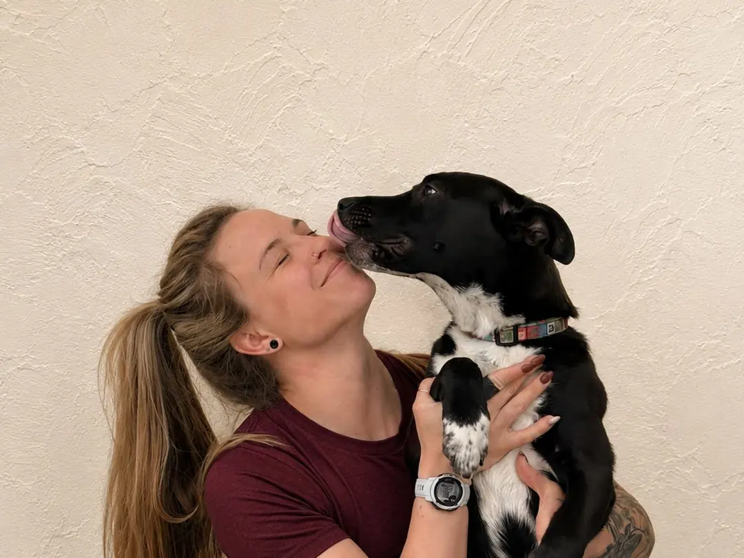 Kaylie holding a black and white dog that is licking her cheek.
